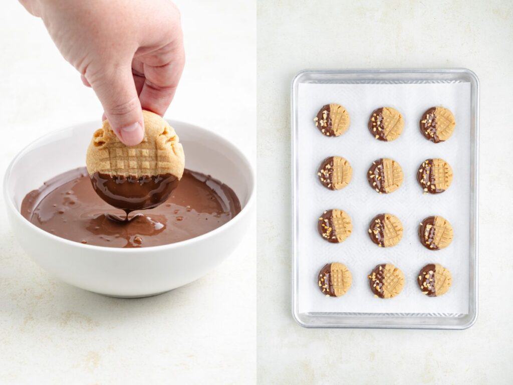 A hand dips a peanut butter cookie in chocolate; finished cookies rest on a parchment-lined baking sheet.