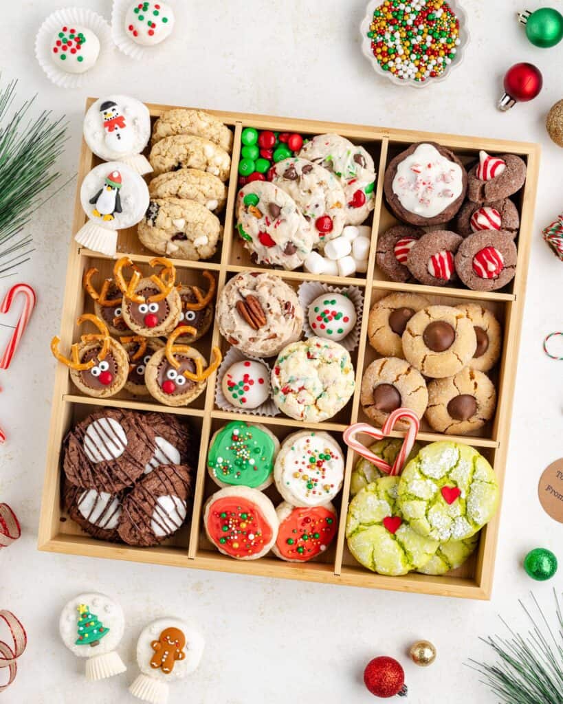 A wooden tray filled with assorted Christmas cookies, including reindeer, peppermint, and frosted shortbread cookies.