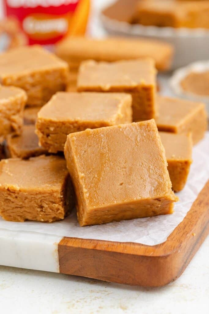 A stack of square, cookie fudge pieces on a wooden serving board.