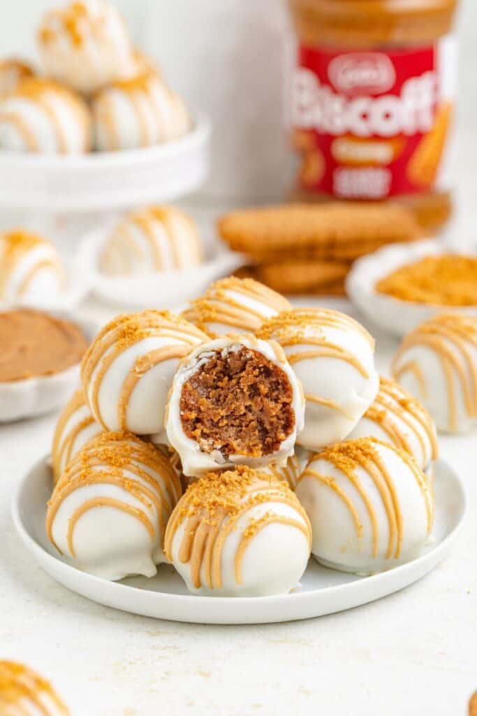 A pile of white chocolate-coated cookie butter truffles drizzled with cookie butter and topped with crumbs.
