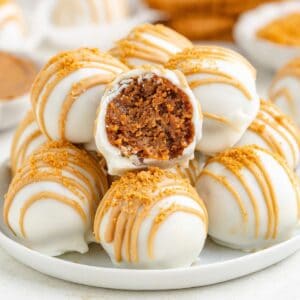 A pile of white chocolate-covered Biscoff truffles, one split open to reveal a brown crumb interior.