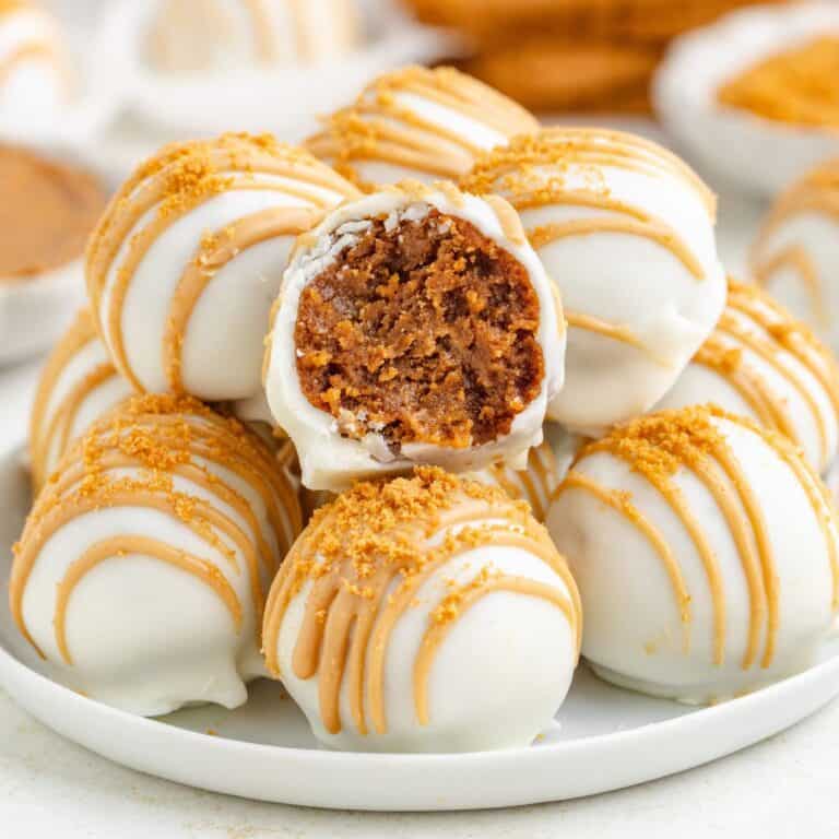 A pile of white chocolate-covered Biscoff truffles, one split open to reveal a brown crumb interior.