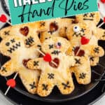 Plate of Voodoo Doll Hand Pies with Halloween icing, candy eyes, skewers, and sign above.